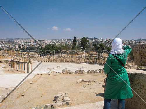 A Young Arabian modern girl wearing a white hijab and green long shirt/ dress looking at the famous historical remains of Jarash on top of a hill