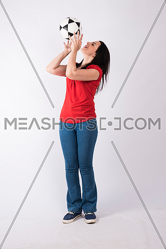 young lady standing and playing with a ball on white background wearing red shirt and jeans