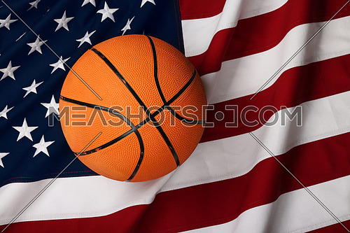 Close up worn orange basketball ball over American flag background, elevated top view, directly above