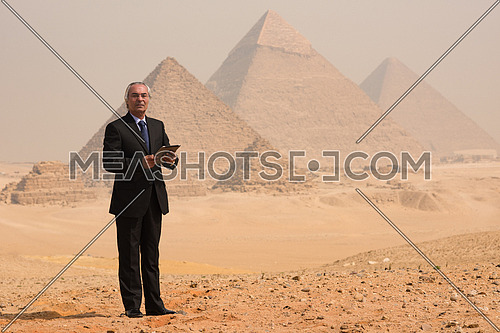 mature arab business man using tablet computer in desert with great giza pyramids in background