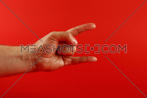 Man hand shoving devil horns gesture, rock music support sign, over red background, side view