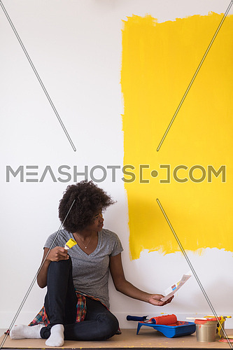 Portrait of a beautiful african american female painter sitting on floor near wall after painting.