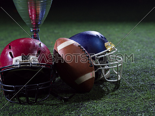 closeup shot of american football,helmets and trophy on grass field at night