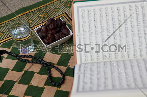 Iftar time Dried Dates, Holy Quran glass of water and tasbih on praying  rug or sejadah in Ramadan concept of Islamic education
