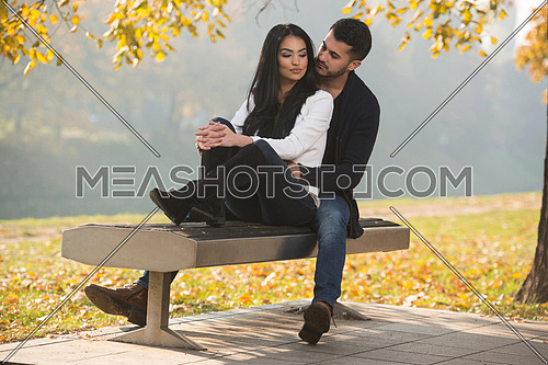 Young Couple Sitting On A Bench In The Beautiful Autumn Day