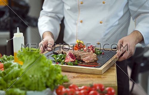 closeup of Chef hands in hotel or restaurant kitchen serving beef steak with vegetable decoration