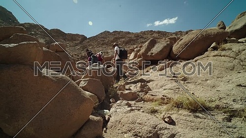Reveal shot for group of tourists climbing big rocks with bedouin guide to explore Sinai Mountain for wadi Freij at day.