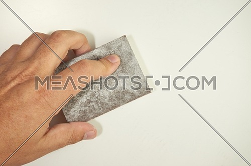 Close view of a hand sanding the wall with a sanding sponge isolated on white. Abrasive tools, DIY, copy space.
