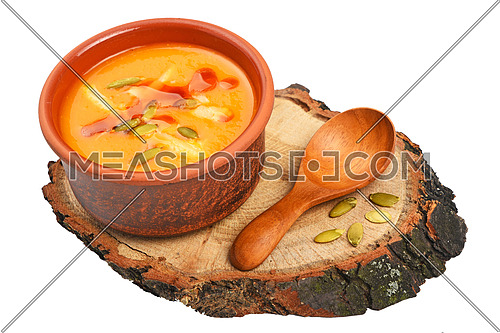 Small ceramic bowl of pumpkin cream soup, wooden spoon, slice of bread and seeds on wood cut isolated on white background, high angle view