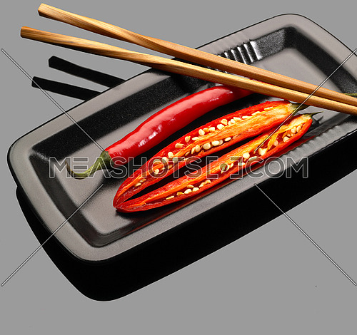 fresh red chili peppers on a plate with chopstikcs over grey reflective surface