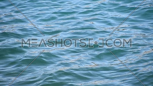 Close up background of blue sea waves and ripples with bright flare sparkles running on water surface