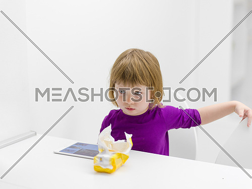 cute little girl eating a cookie while playing games on tablet computer at home