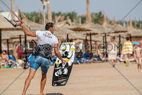 Kite Surfer waling on beach wearing surfing set by day.