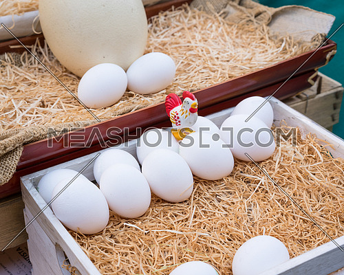 White chicken eggs leaning on straw in wooden basket