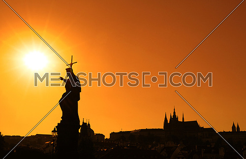 Sunset backlit silhouettes of statues and roofs of cityscape skyline at Charles Bridge in Prague, Czech Republic