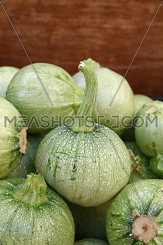 Close up fresh new green baby round zucchini in wooden box on retail display of farmers market, high angle view