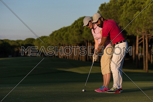 male golf instructor teaching female golf player, personal trainer giving lesson on golf course