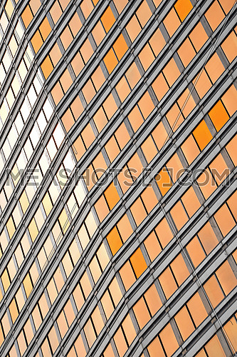 Orange colored glass windows of modern business office building at sunset in evening, diagonal perspective, low angle view