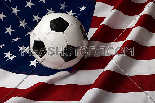 Close up worn black and white soccer football ball over American flag background, high angle view