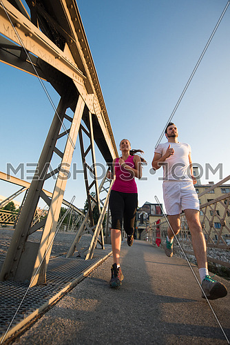 urban sports, healthy young couple jogging across the bridge in the city at sunny morning