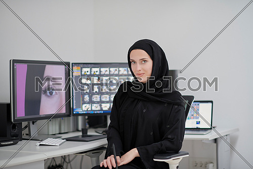 Portrait of young muslim female graphic designer. Hijab girl with the two monitors in background showing her work. Technology concept