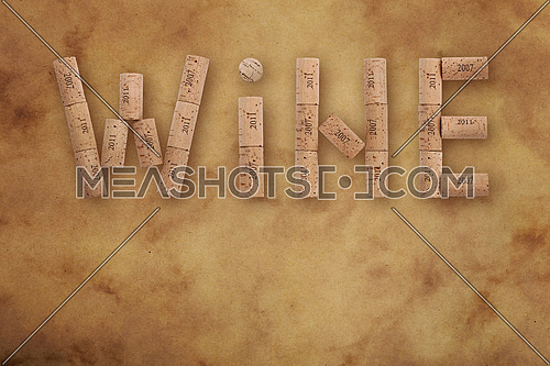 Word WINE shaped by natural wooden wine bottle corks of different vintage years over background of brown paper parchment