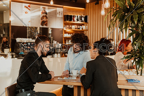 A group of friends hanging out in a cafe, and among them is a tablet. Happy young people sitting in a restaurant using tablets