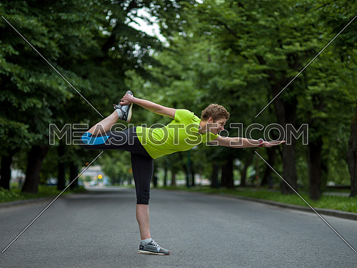healthy female runner warming up and stretching in city park before morning training