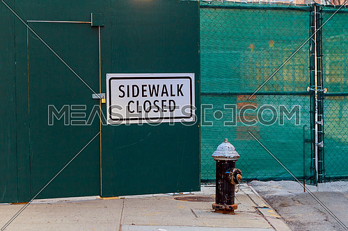 SIDEWALK CLOSED sign posted on green construction wall barrier. Horizontal.