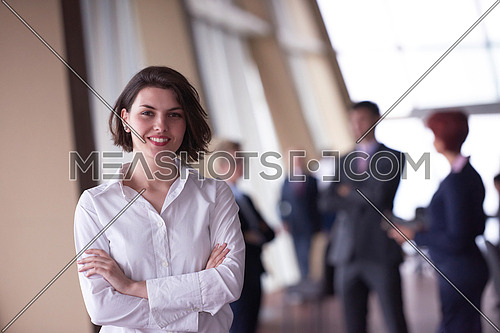 Smilling young business woman in front her team blured in background. Group of young business people. Modern bright  startup office interior.