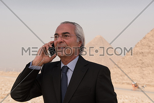 mature arab business man speeking over smartphone  with egyptian pyramids in background
