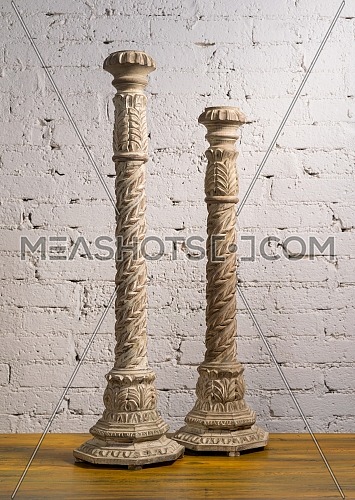 Two white vintage wooden candlesticks on a background of wooden floor and white painted brick wall