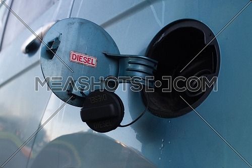 Close up on the open cap of a fuel tank of a vehicle with red sign for Diesel and drips on the bodywork in a low angle view