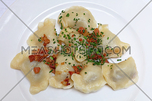 Plate of pierogi or varenyky stuffed filled dumplings with bacon crisps and green chive onion, traditional East Europe cuisine meal popular in Poland, Ukraine, Slovakia and Russia, close up, elevated top view