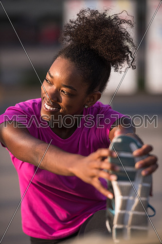 young beautiful African American woman doing warming up and stretching with her leg raised to the bridge before the morning run with the sunrise in the background