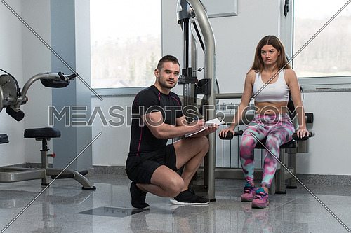 Personal Trainer Showing Young Woman How To Train Triceps On Machine In The Gym