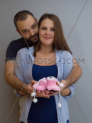 young  pregnant couple holding newborn baby shoes isolated on white background in family and parenthood concept