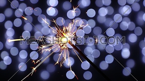 Close up one firework sparkler over black background with defocused blue bokeh, low angle side view