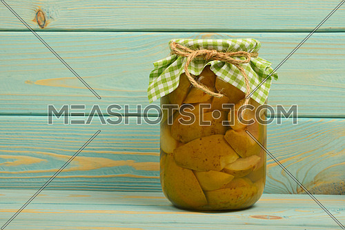 One glass jar of homemade pear compote with green checkered textile top decoration at blue painted vintage wooden surface