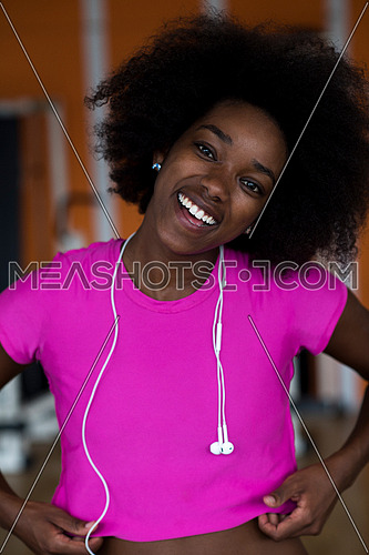 afro american woman running on a treadmill at the gym while listening music on earphones