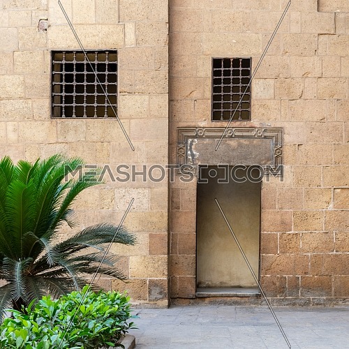 Ancient external old decorated bricks stone wall with two windows and opened door leading to Ottoman era Beit El Sehemy historical building, Cairo, Egypt