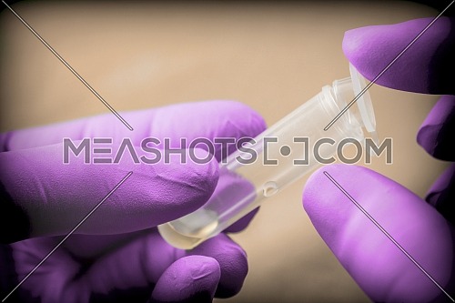 Scientist with pink latex gloves manipulates vial in laboratory, conceptual image
