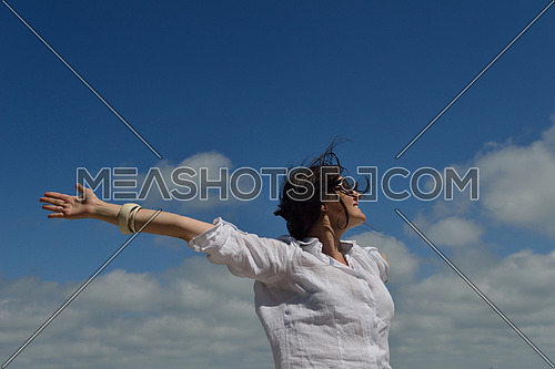 Happy  young woman with spreading arms, blue sky with clouds in background  - copyspace