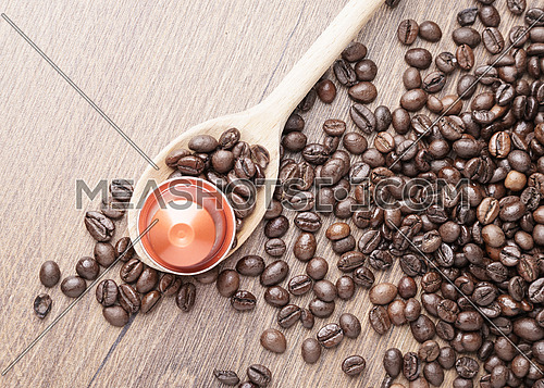 Coffee capsule on wooden spoon and roasted coffee beans on wooden background,top view,close up.