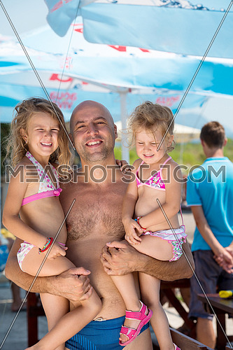 portrait of young happy father having fun with his cute little daughters while holding them in his hands by the sea during Summer vacation  Healthy family holiday concept