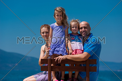 portrait of young happy family with cute little daughters having fun on a bench by the sea during Summer vacation  Healthy family holiday concept