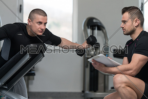 Personal Trainer Working With A Young Man At The Gym Writing Notes On A Clipboard In A Health And Fitness Concept