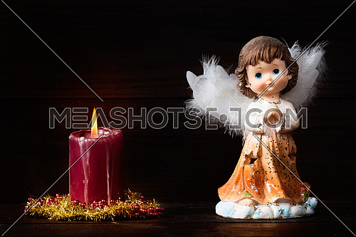 Christmas greeting card with candle and angels on wooden background.