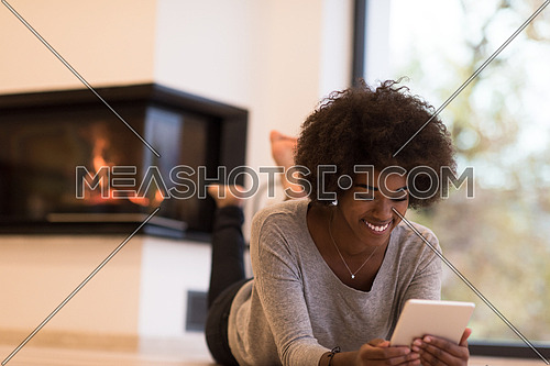 beautiful young black women using tablet computer on the floor of her luxury home in front of fireplace at autumn day