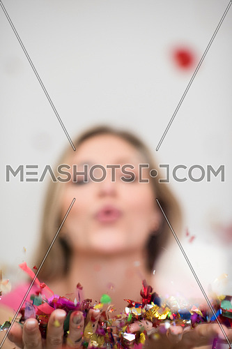 beautiful young woman celebrating new year and chrismas party while blowing confetti decorations to camera